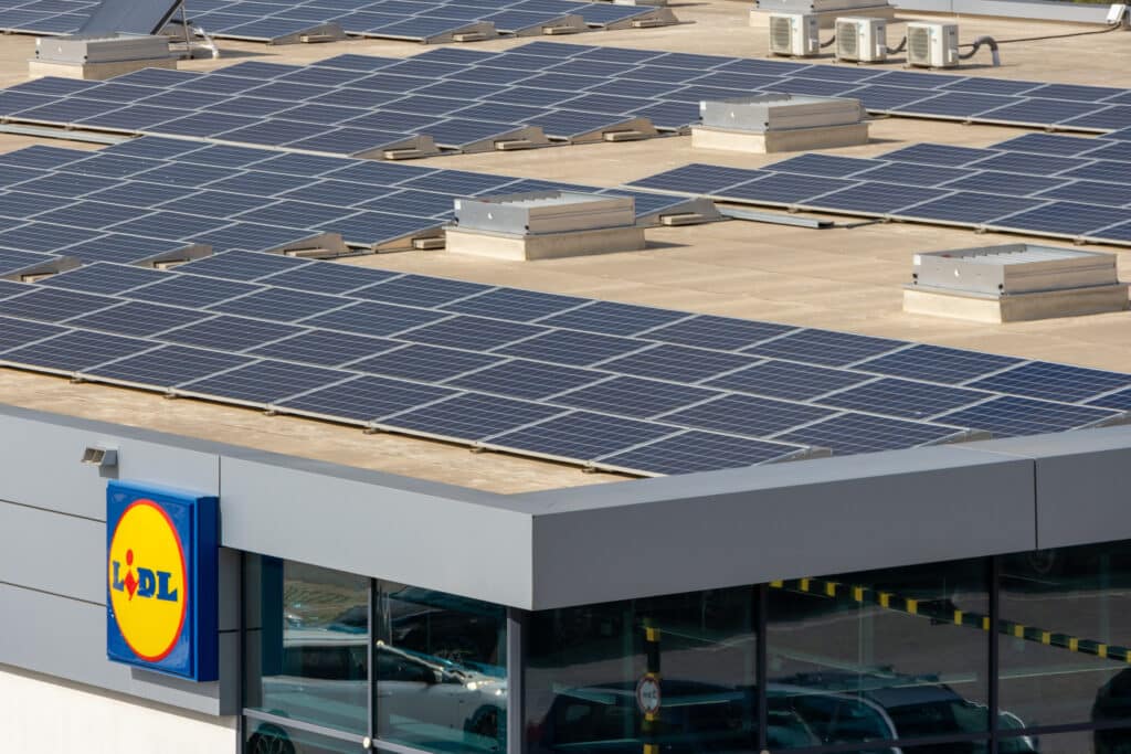 Panneaux Solaires sur Toit de Magasin Lidl : Énergie Verte Toit d'un magasin Lidl couvert de nombreux panneaux solaires et unités de climatisation. Reflets de voitures dans les fenêtres.