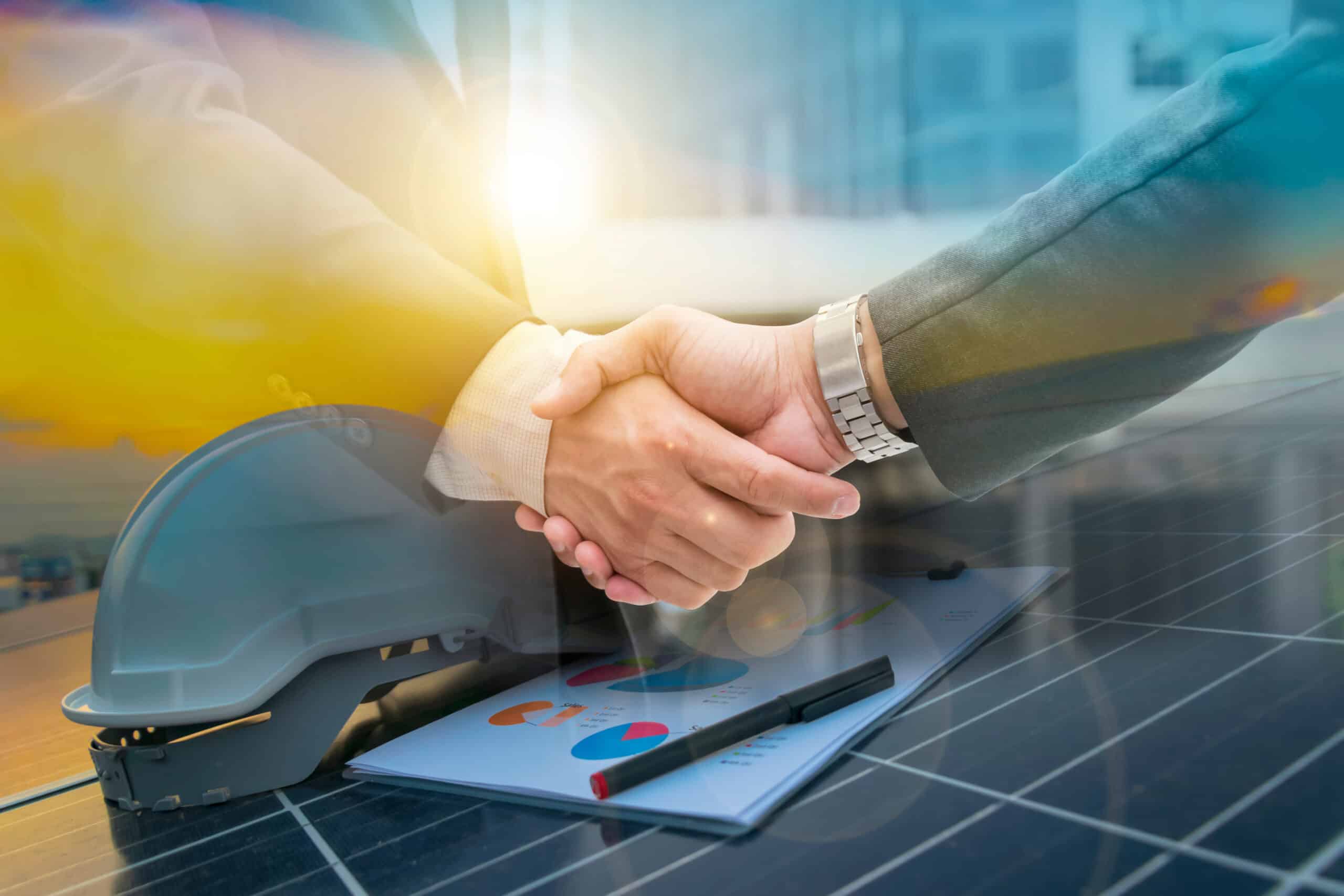 Deux personnes se serrent la main, superposées sur des panneaux solaires, un casque de chantier et un rapport de "Sales". Accord dans l'énergie durable.