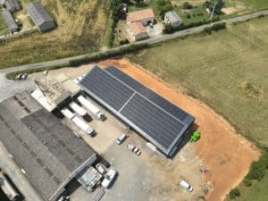 Vue aérienne d'un site logistique avec camions, entrepôts anciens et nouveau bâtiment équipé d'un grand champ de panneaux solaires.