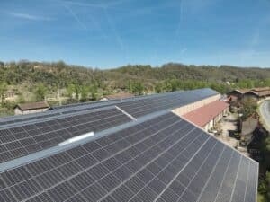 Toit industriel couvert de panneaux solaires, dominant un paysage vallonné et boisé par un ciel bleu clair avec traînées de condensation.