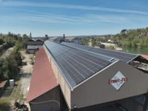 Vue aérienne d'un grand bâtiment industriel avec des panneaux solaires recouvrant une grande partie du toit, portant le logo "À TOUT-FER RÉCUPÉRATION".