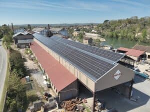 Vue aérienne d'un site industriel avec un toit couvert de panneaux solaires. Logo 'À TOUTE RÉCUPÉRATION' visible. Rivière et colline boisée en arrière-plan.