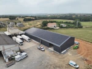 Vue aérienne d'un site logistique agricole avec camions et grande toiture recouverte de panneaux solaires. Un van porte le texte "Spécialiste en énergie photovoltaïque".