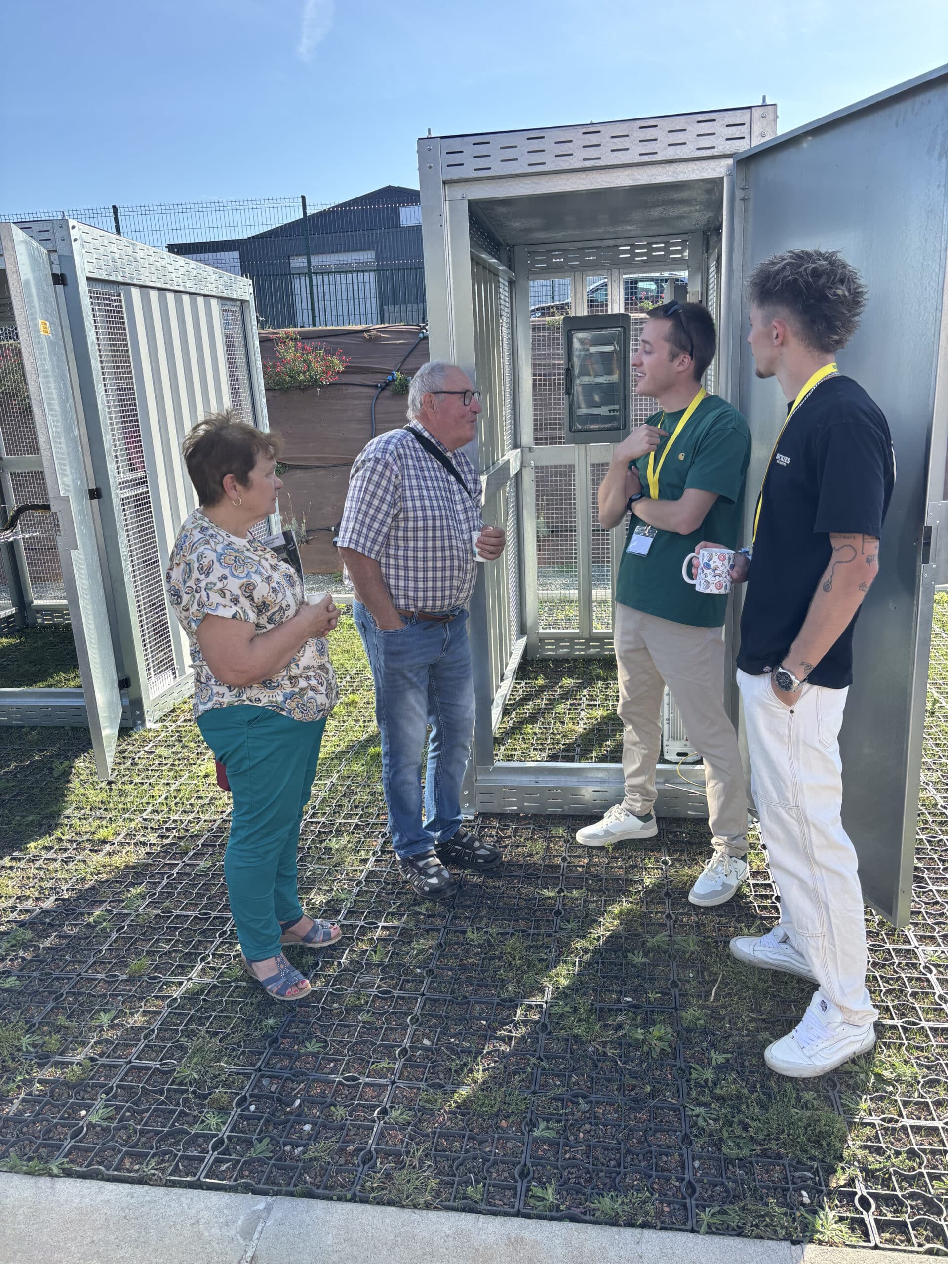 Présentation technique d'armoires électriques métalliques en extérieur avec quatre personnes en discussion.