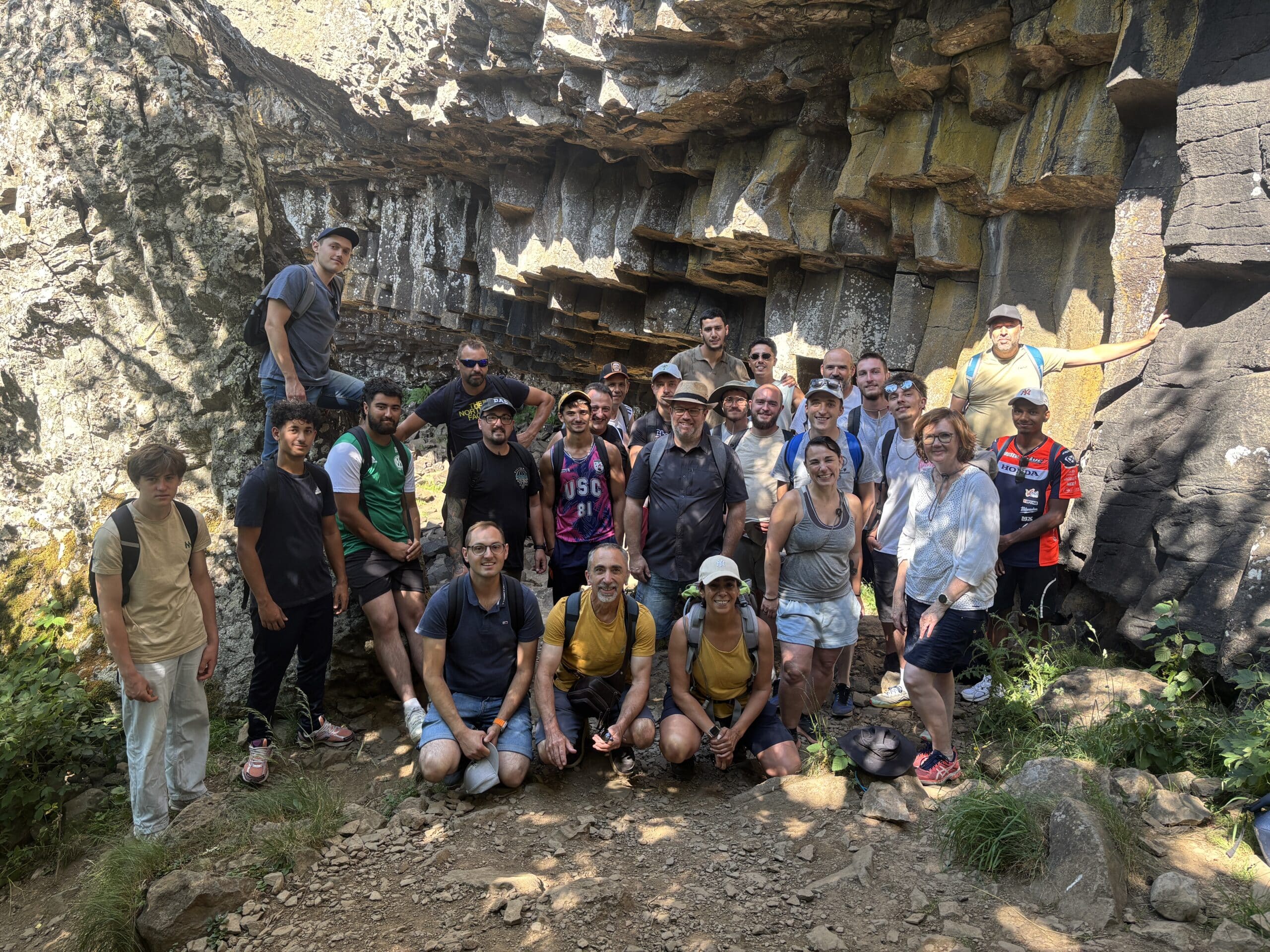 Groupe de randonneurs souriants devant des colonnes basaltiques dans une formation rocheuse naturelle.